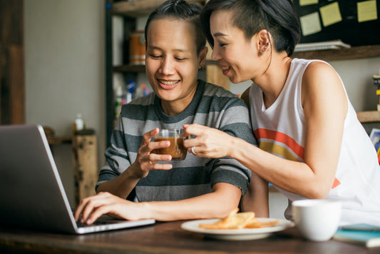Queer woman in white rainbow top handing partner cup of coffee as they discuss why you should go to therapy before your next relationship