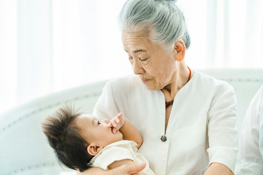older asian woman holding baby with dark brown hair representing the generational trauma that can pass down through epigenetics