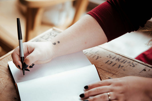 Women with black nail polish writing in notebook about suicide prevention with a semicolon tattooed on her wrist